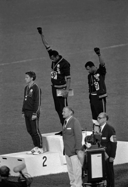 Photographie prise le 16 Octobre 1968 aux Etats-Unis du podium après une épreuve de sprint aux JO. C'est un moment historique dans le sport : à la première position, au centre, Tommie Smith,  et à la troisième, en haut à droite, John Carlos, tendent leur point vers le ciel.
